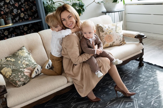 Glückliche Mutter sitzt mit zwei süßen Söhnen in stylischer Kleidung auf dem Sofa
