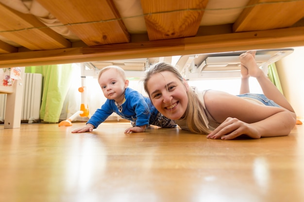 Glückliche Mutter und Baby, die auf dem Boden liegen und unter das Bett schauen