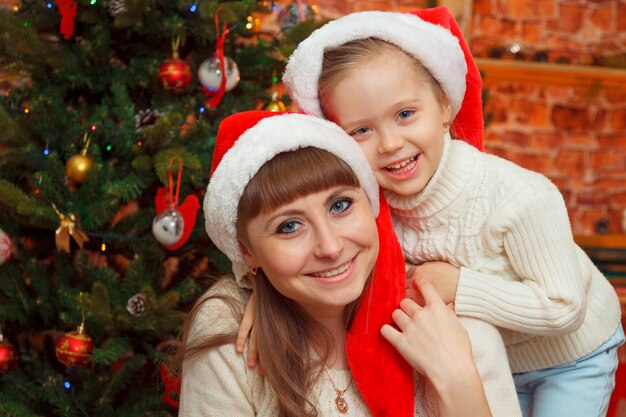 Glückliche Mutter-und Baby-Tochter nahe durch Weihnachtsbaum am Weihnachtsabend