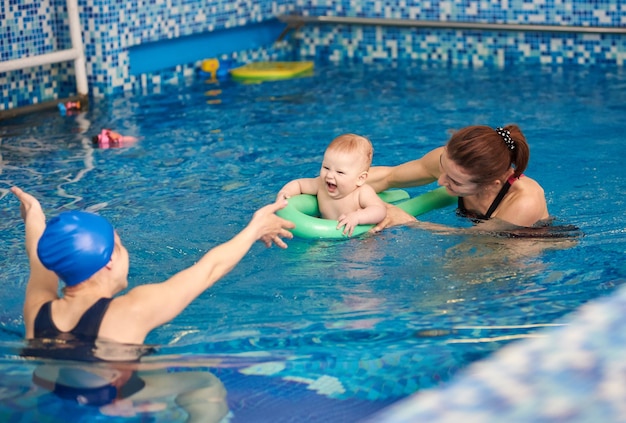 Glückliche Mutter und ihr Sohn lachender kleiner Junge, der Spaß beim Schwimmen hat, trainiert mit Trainer im Planschbecken