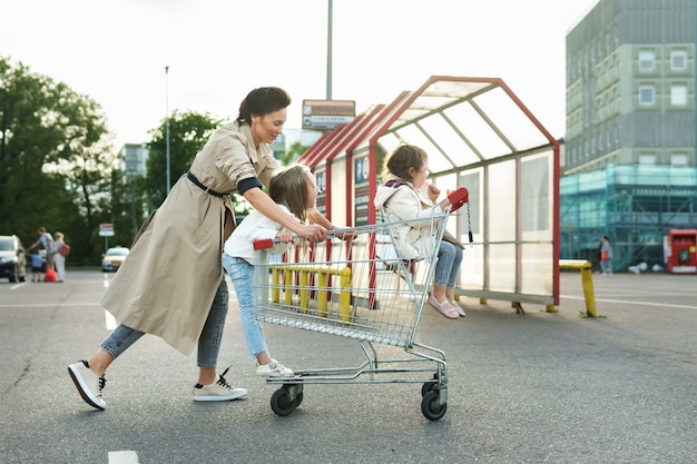 Glückliche Mutter und ihre Töchter haben Spaß mit einem Einkaufswagen