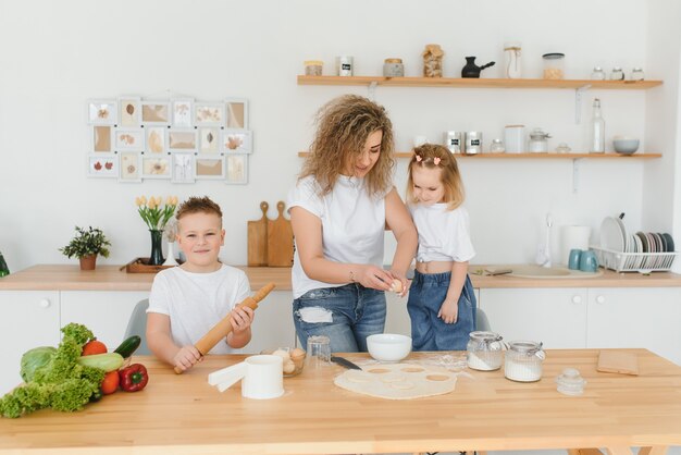 Glückliche Mutter und Kinder mischen Zutaten für hausgemachten Kuchen, Kuchen oder Keksteig in der Küche.