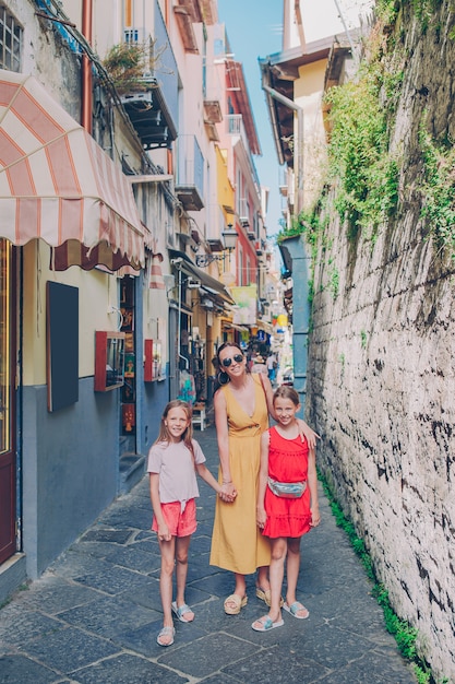 Glückliche Mutter und kleine entzückende Kinder auf gemütlicher Straße während des italienischen Urlaubs.