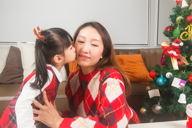 Glückliche Mutter und kleine Tochter, die Weihnachtsbaum und Geschenke zu Hause verzieren