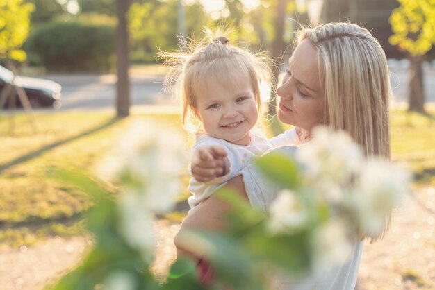 Glückliche Mutter und kleine Tochter im Park an einem sonnigen Tag bei Sonnenuntergang Mutter und Kind im Freien Konzept der Zärtlichkeit Familie alleinerziehende Mutter Blumen lächelt Umarmungen psychische Gesundheit Harmonie Urlaub