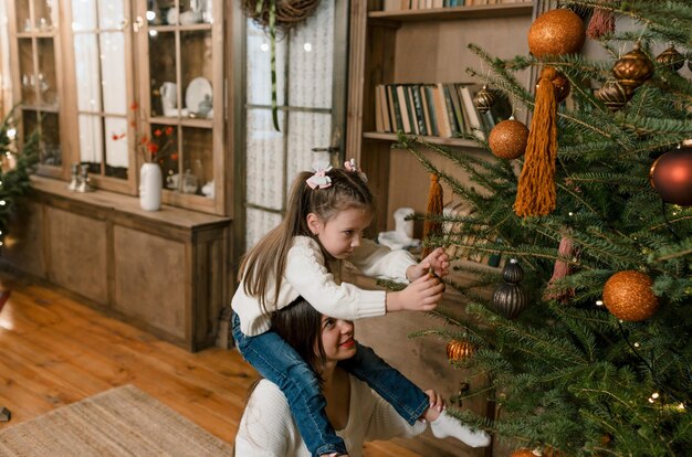 Glückliche Mutter und kleine Tochter schmücken den Weihnachtsbaum zu Hause. Glückliche Familie. Das Konzept von Frohe Weihnachten und Neujahr.