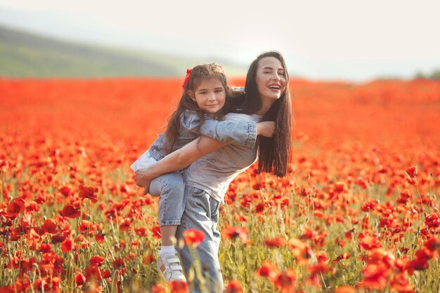 Glückliche Mutter und kleine Tochter spielen zusammen und haben Spaß im Mohnfeld beim Wandern in der Natur