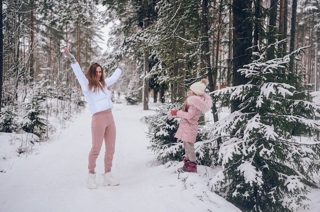 Glückliche Mutter und kleines süßes Mädchen in rosa warmer Oberbekleidung beim Spielen einer Schneeballschlacht, die Spaß hat