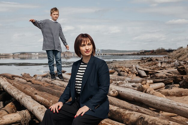 Glückliche Mutter und Sohn am Flussufer stehen auf Baumstämmen in gestreiften Westen.
