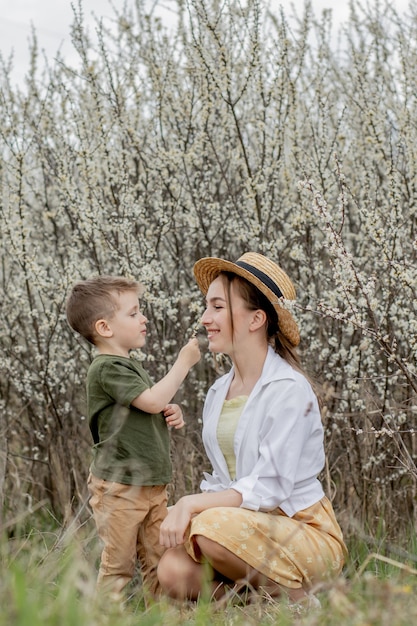 Glückliche mutter und sohn, die spaß zusammen haben. mutter umarmt sanft ihren sohn. im hintergrund blühen weiße blumen. muttertag.