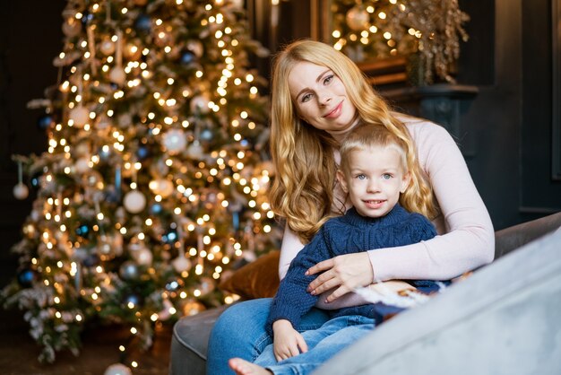 Glückliche Mutter und Sohn sitzen auf dem Sofa vor dem Hintergrund eines geschmückten festlichen Weihnachtsbaumes