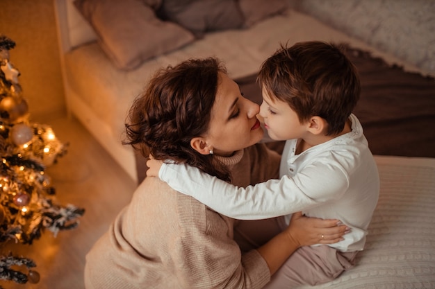 Glückliche Mutter und Sohn zu Hause im Schlafzimmer in der Nähe des Weihnachtsbaumes