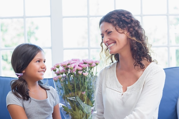 Glückliche Mutter und Tochter, die auf der Couch mit Blumen sitzt