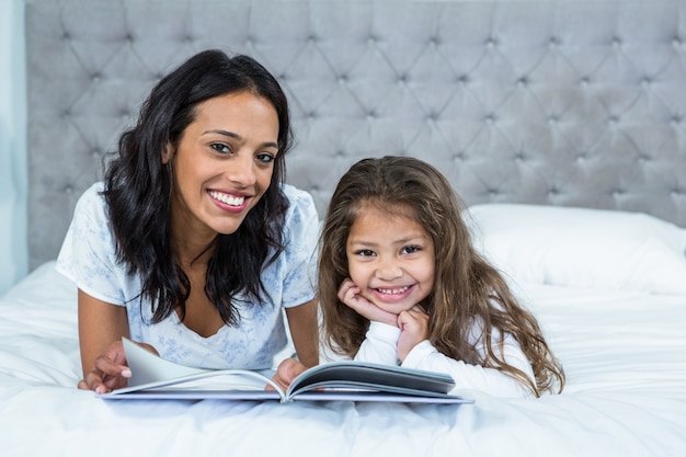 Glückliche Mutter und Tochter, die ein Buch auf dem Bett liest