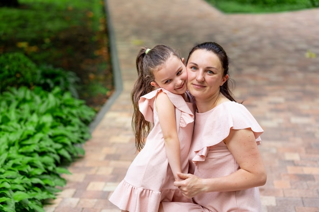 Glückliche Mutter und Tochter im Alter von 5-6 Jahren gehen im Sommer im Park spazieren, Mutter umarmt ihre Tochter, das Konzept einer glücklichen Familie, die Beziehung von Mutter und Kind, Muttertag