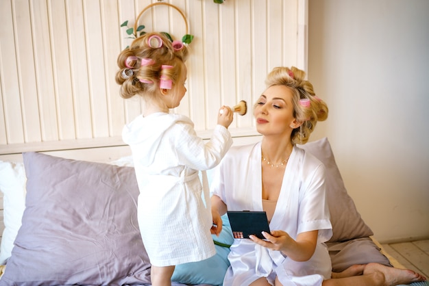 Glückliche Mutter und Tochter schminken sich auf dem Bett im Schlafzimmer