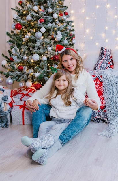 Glückliche Mutter und Tochter sitzen zwischen Geschenkboxen auf dem Hintergrund des Weihnachtsbaums.