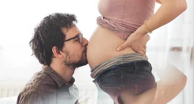 Glückliche Mutter und Vater umarmen den schwangeren Bauch aus nächster Nähe