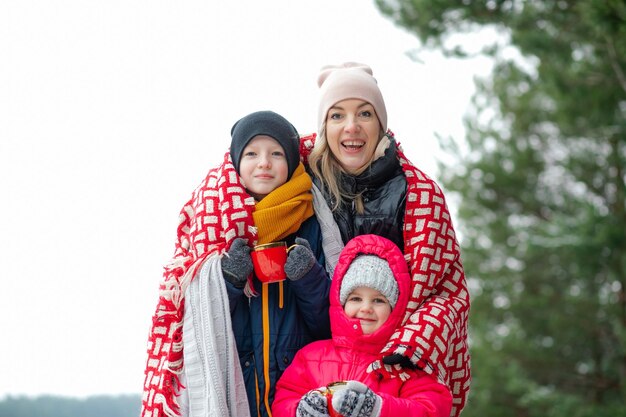 Foto glückliche mutter und zwei kleine kinder im winterwald, familienausflug außerhalb der stadt, die leute wärmen sich mit ho auf