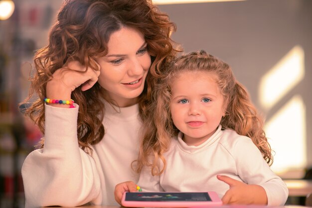 Glückliche Mutterschaft. Freundliches Baby, das Lächeln auf ihrem Gesicht hält, während es direkt in die Kamera schaut