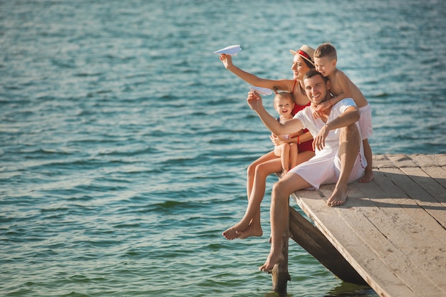 Glückliche nette Familie am Pier nahe dem Wasser, das Spaß hat. Entzückende Kinder, die mit ihren Eltern spielen