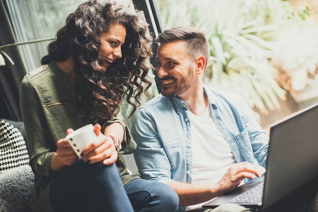 Glückliche nette Paare in der Liebe mit trinkendem Kaffee und dem Lächeln des Laptops