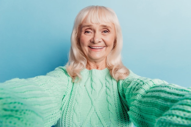 Glückliche reife Dame, die ein Selfie auf blauem Hintergrund macht