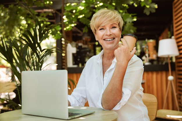 Glückliche reife Frau, die an einem Café mit Laptop-Computer sitzt