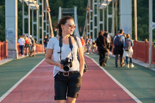 Glückliche reife Frau in Sonnenbrille mit Rucksack Fotokamera zu Fuß