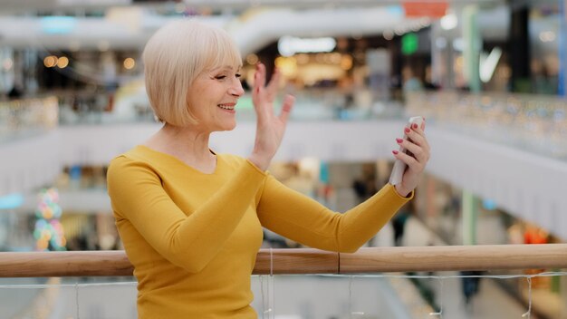 Glückliche, reife Frau mittleren Alters hält ein Smartphone in der Hand und spricht über einen Videoanruf mit einer mobilen App für