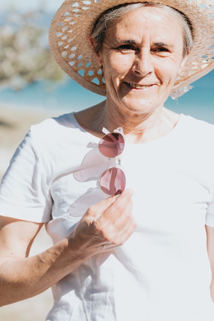 Glückliche reife Frau von 50 Jahren am Strand mit trendiger Sonnenbrille und Hut