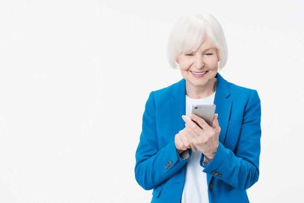 Glückliche reife Seniorin, die Smartphone mit mobilen Online-Apps auf weißem Hintergrund hält