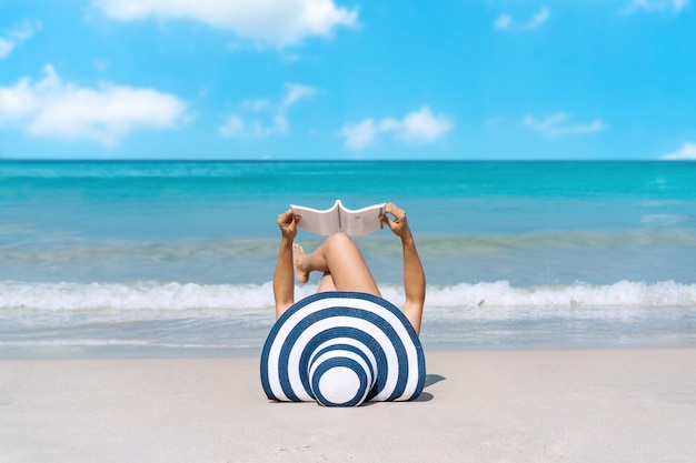 Glückliche Reisende Asiatin legt sich hin, um im Urlaub ein Buch am tropischen Strand zu lesen. Sommer am Strandkonzept.