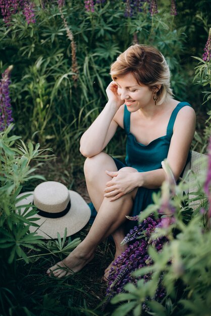 Glückliche romantische Frau in einem Feld der lila Lupinenblumen flirtet und lächelt.