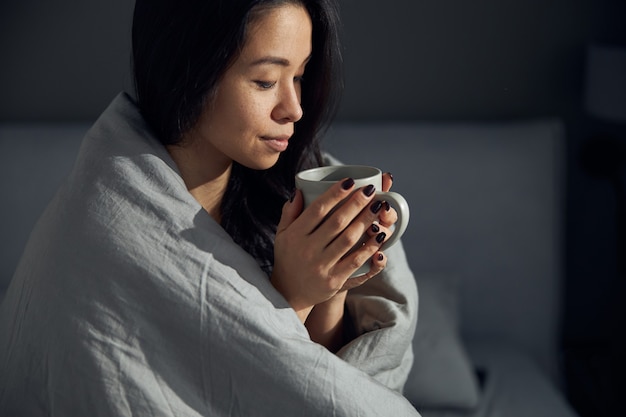 Glückliche schöne asiatische Frau hält eine Tasse und genießt ihren Morgenkaffee