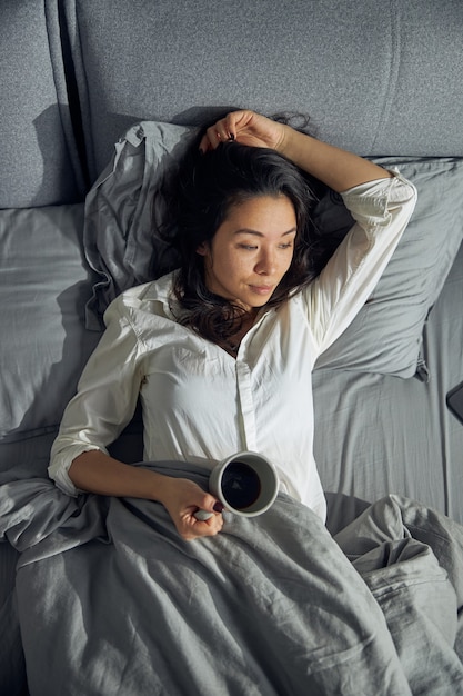 Glückliche schöne asiatische Frau hält eine Tasse und genießt ihren Morgenkaffee