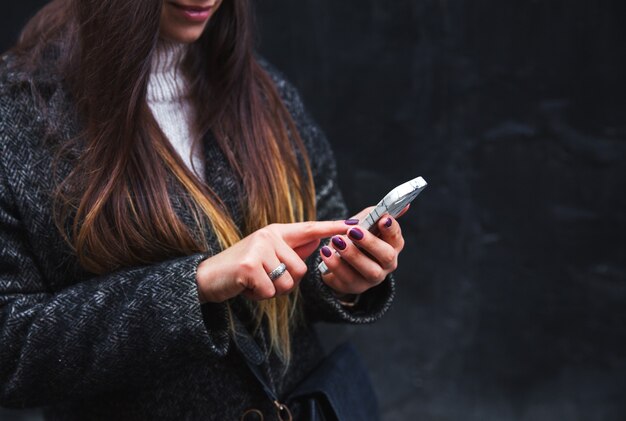 Glückliche schöne Frau, die auf Handy auf einer schwarzen Wand spricht