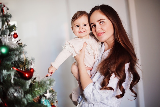 Glückliche schöne Frau, die Spaß mit ihrer kleinen Tochter nahe dem Weihnachtsbaum hat