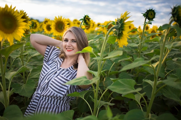 Glückliche schöne Frau mittleren Alters freut sich und genießt das Sonnenblumenfeld, das an einem sonnigen Tag blüht