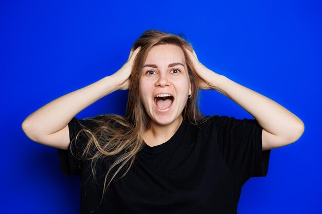 Glückliche schöne Frau ohne Make-up in einem schwarzen T-Shirt, das verschiedene Emotionen auf blauem Hintergrund zeigt Natürliche weibliche Schönheit ohne Kosmetik Natürlichkeit Das Konzept der Schönheit