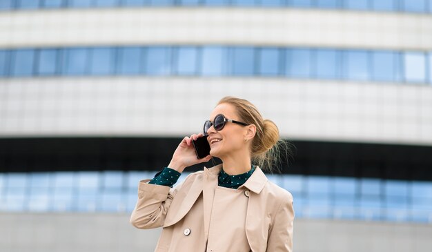 Glückliche schöne Geschäftsfrau mit Sonnenbrille, die am Telefon spricht