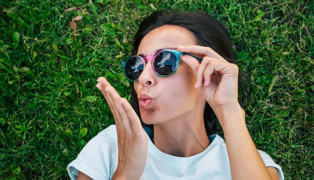 Glückliche schöne Hipster Frau in der coolen Sonnenbrille hat Spaß, während sie auf dem Rasen liegt