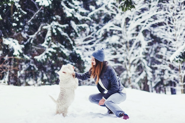 Glückliche schöne junge Frau, die an einem Wintertag zu ihrem weißen Terrier des Hundes spielt. Freundschaft, Haustier und Mensch.