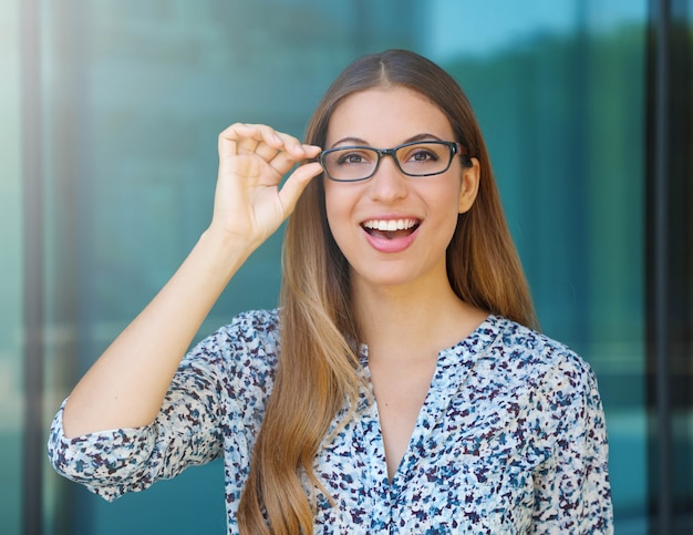 Glückliche schöne junge Frau hält ihre Brille und schaut auf Kamera im Freien