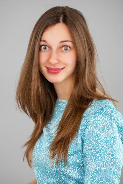 Glückliche schöne junge Frau in einem türkisfarbenen Kleid auf einem grauen Hintergrund Studio-Porträt