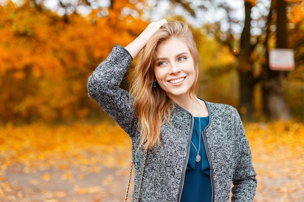 Glückliche schöne junge Frau mit einem Lächeln in einem Mantel am Herbsttag