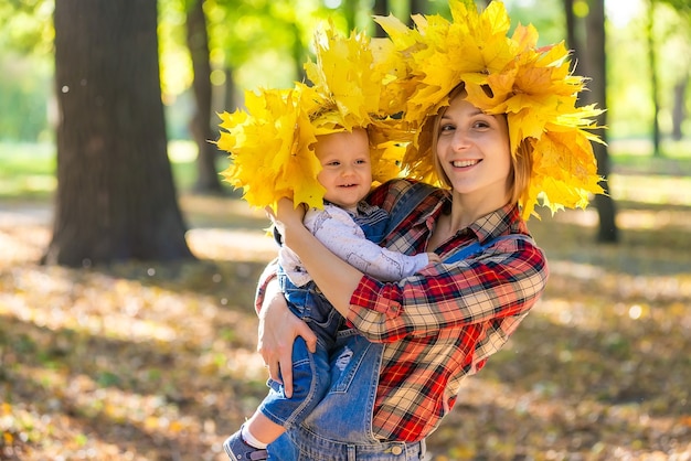 Glückliche schöne junge Mutter, die ein Kind hält, das im Herbst im Park spaziert.