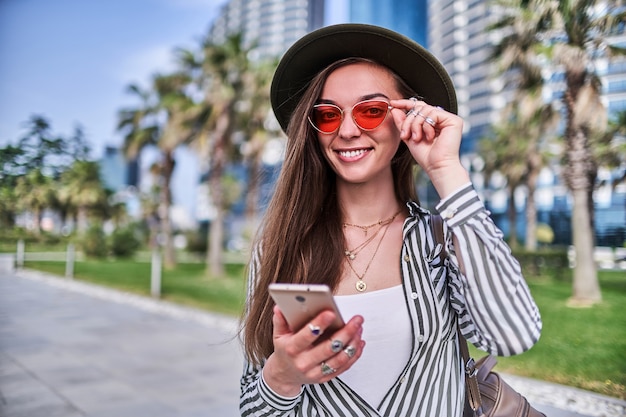 Glückliche schöne lächelnde modische Hipsterfrau im Freien