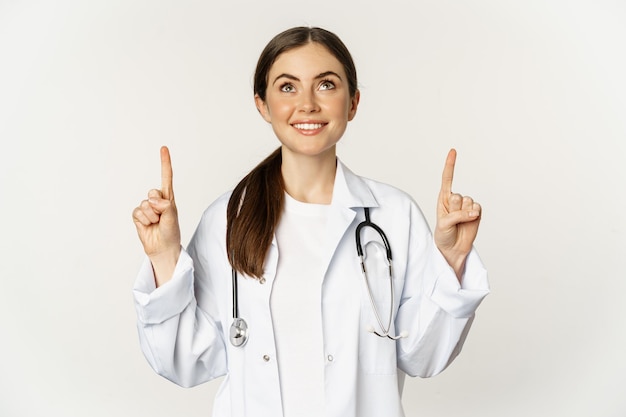 Glückliche schöne Ärztin Ärztin, die mit dem Finger nach oben zeigt und Werbung zeigt, die über Weiß steht ...