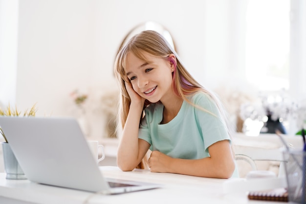 Glückliche Schülerin des kleinen Mädchens, die zu Hause Laptop verwendet